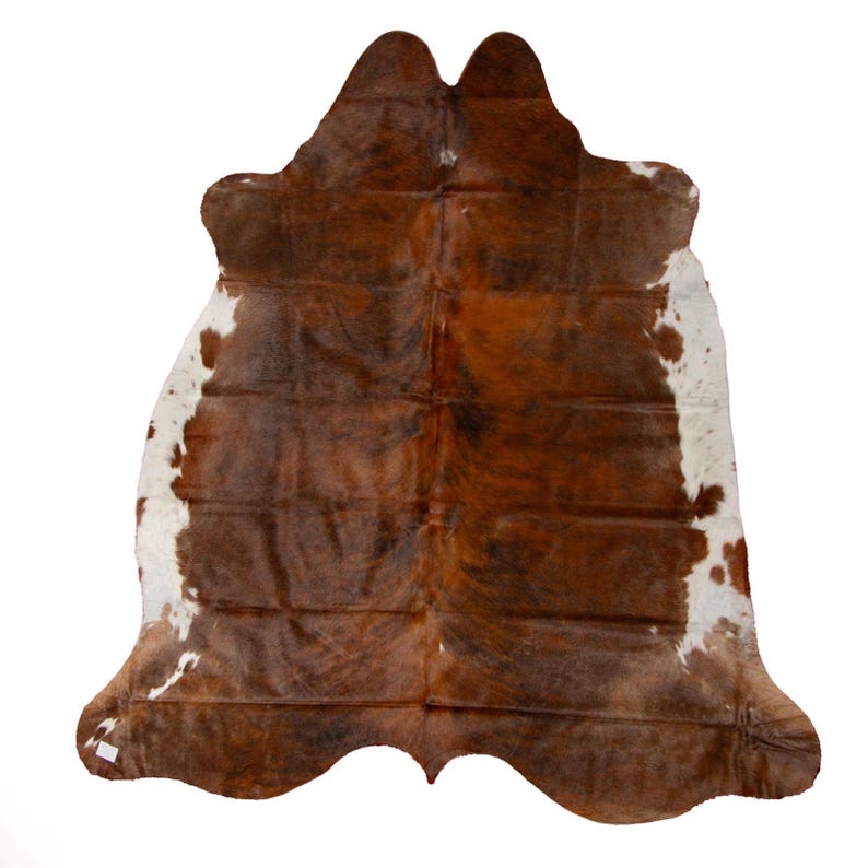 May include: A brown and white cowhide rug with a natural, rustic look. The hide is soft and supple, with a unique pattern of brown and white patches.