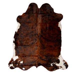 May include: A brown and white cowhide rug with a natural, rustic look. The hide is soft and supple, with a variety of shades of brown and white.