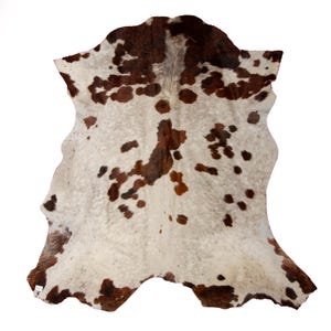 May include: A white cowhide rug with brown and reddish-brown spots. The rug is folded in half and has a natural, rustic look.