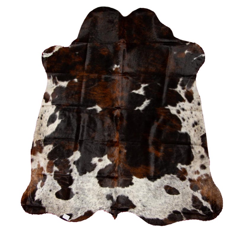 May include: A brown, black, and white cowhide rug with a natural, irregular shape. The hide has a patchwork pattern of different shades of brown and black, with white spots scattered throughout.