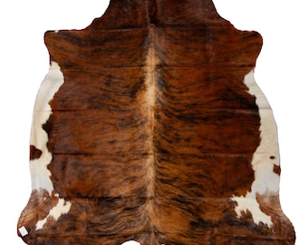 May include: A brown and white cowhide rug with a natural, irregular shape. The hide has a variety of brown and white markings.