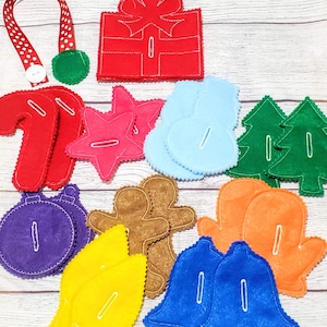 May include: A set of felt Christmas ornaments with various shapes and colors, including a red present, a green tree, a blue snowman, a purple ornament, a yellow light, a brown gingerbread man, an orange mitten, and a red candy cane.