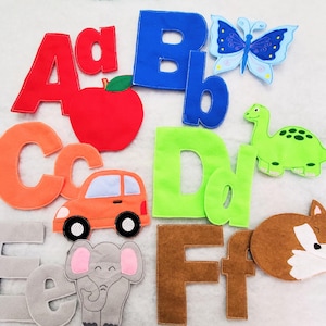May include: A set of felt alphabet letters A through F in various colors, including red, blue, orange, lime green, gray, and brown. The set features embroidered appliques of an apple, a butterfly, a car, a dinosaur, an elephant, and a fox.