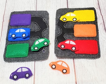 May include: A felt quiet book with a road theme. The book has two pages with cars, traffic lights, and roads. The cars are red, green, yellow, orange, and purple.