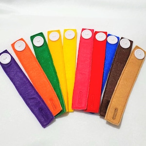 May include: Set of ten colorful felt wristbands with white buttons. The wristbands are in the colors purple, orange, green, yellow, red, blue, brown, and beige.