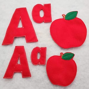 May include: Two sets of red felt fabric cutouts, each featuring an uppercase letter A, a lowercase letter a, and a red apple shape with a green leaf. Each piece is outlined with white stitching along the edges, creating a soft, flat, educational set.