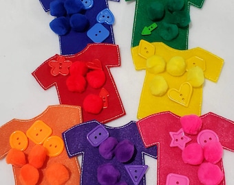 May include: Six felt t-shirts in different colors, each with a different button, pom-pom, and shape. The colors are blue, red, yellow, orange, purple, and pink.