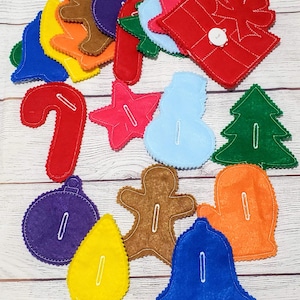 May include: A set of felt Christmas ornaments in various shapes and colors, including a star, a snowman, a tree, a gingerbread man, a bell, a candy cane, a light bulb, a mitten, a present, and an ornament. The ornaments are all sewn with white thread and have a button sewn on the back.