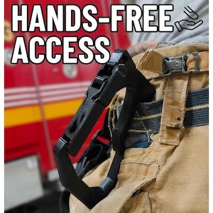 Puede incluir: Un clip utilitario negro, rígido y en forma de D sujeto a un pantalón de trabajo color canela. El texto HANDS-FREE ACCESS está impreso en blanco en la parte superior, junto a un pequeño icono de una mano y un clip. La superficie es texturizada.