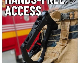May include: A black, rigid, D-shaped utility clip attached to tan work trousers. The text HANDS-FREE ACCESS is printed in white at the top, accompanied by a small icon of a hand and a clip. The clip features a textured, layered surface.