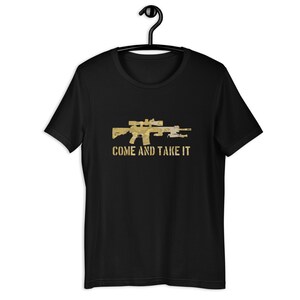May include: Black t-shirt with a gold-colored graphic of a rifle with a scope and the text "COME AND TAKE IT". The shirt is hanging on a black hanger.
