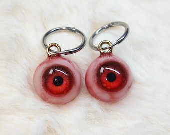 May include: Two red eyeball keychains with black pupils and silver key rings. The eyeballs are made of a clear resin with a red and white design.