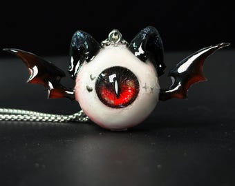 Collar gótico con forma de ojo de murciélago y colgante vertical rojo y blanco con forma de oreja de gato.