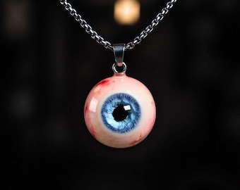 May include: A pendant necklace featuring a realistic eyeball charm. The charm has a blue iris, a black pupil, and red veins. The pendant hangs from a silver chain, creating a unique and eye-catching accessory.