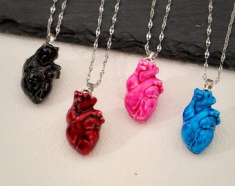 May include: Four silver chains with anatomical heart pendants. The hearts are in black, red, pink, and blue.