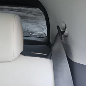 Op de afbeelding: Een witte autostoel met een zwarte hoofdsteun en een grijze veiligheidsgordel.