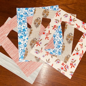 May include: A collection of decorative picture frames with various floral and geometric patterns. The frames feature designs in red, blue, beige, and white, creating a colorful and artistic display. The frames are arranged on a wooden surface.