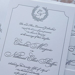 May include: Elegant wedding invitations with embossed gray lettering on white cardstock. The design includes the names of the couple, the date, and a decorative wreath with initials. The invitations are for Charlotte Marjorie and Nathaniel Elliot Schaffer.