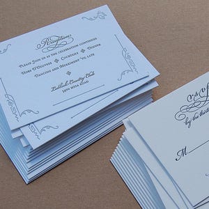 May include: Stacks of white wedding reception invitations and RSVP cards. The invitations have elegant script and decorative flourishes. The reception card includes details like "Hors D'oeuvres" and "Dancing and Merriment".