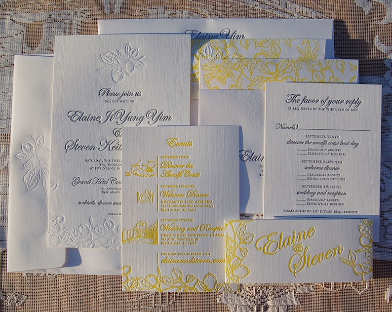 May include: A collection of white wedding stationery with embossed floral designs and yellow accents. Includes invitations, reply cards, and place cards. The text includes names, dates, and event details.