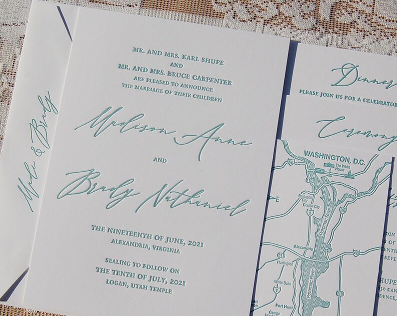 May include: White wedding invitation suite with teal script. The invitation includes the names Madison Anne and Brady Nathaniel, along with the wedding date and location in Alexandria, Virginia. A map of Washington, D.C. is also included.