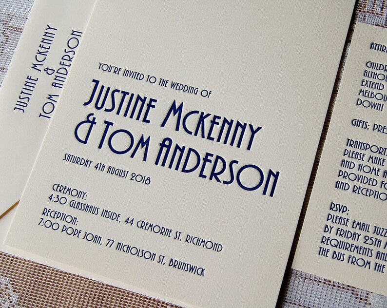 May include: Cream-colored wedding invitation with navy blue text. The invitation reads "You're invited to the wedding of Justine Mckenny & Tom Anderson" with ceremony and reception details. The date is Saturday, 4th August 2018.