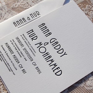 May include: A white wedding invitation with black text, featuring the names "Anna & Nur" on the envelope and the invitation. The invitation includes the names "Anna Gaddy & Nur Mohammed", date, time, and location: Milwaukee Museum of Art.