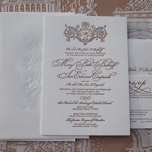 May include: Elegant wedding invitation suite in ivory with brown script. The invitation features ornate calligraphy and a decorative crest. Includes an RSVP card and envelopes, perfect for a formal event.
