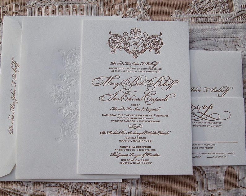 May include: Elegant wedding invitation suite in ivory with brown script. The invitation features ornate calligraphy and a decorative crest. Includes an RSVP card and envelopes, perfect for a formal event.