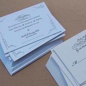 May include: Stacks of white wedding reception invitations and RSVP cards. The invitations have elegant script and decorative flourishes. The reception card includes details like "Hors D'oeuvres" and "Dancing and Merriment". The RSVP cards have a space for the recipient's name.