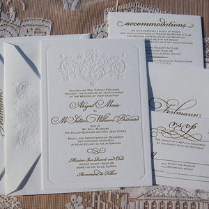 May include: Elegant white wedding invitation suite with gold script and embossed floral details. Includes invitation, RSVP card, accommodations card, and envelopes. The invitation text includes the names Abigail Marie and M. Milton William Burnard.