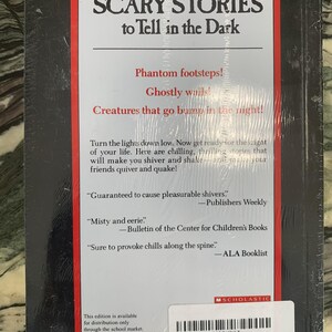 Puede incluir: Un libro de bolsillo titulado "SCARY STORIES to Tell in the Dark" con una cubierta negra y texto rojo y blanco. La contraportada presenta citas y una descripci&oacute;n que promete historias escalofriantes. El libro est&aacute; sellado en pl&aacute;stico.