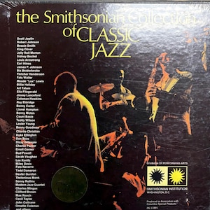 May include: A vintage vinyl record album titled "The Smithsonian Collection of Classic Jazz." The cover features a silhouette of jazz musicians playing instruments in shades of yellow and orange against a dark background. The album lists jazz legends.