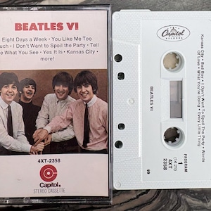 May include: A vintage cassette tape of The Beatles' album "Beatles VI" with the Capitol Records logo. The album cover features a photo of the band members. The cassette tape is white with the album title and tracklist printed on it.