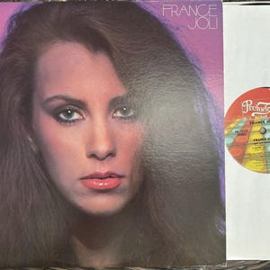 May include: A vinyl record album cover featuring a portrait of France Joli against a purple gradient background, with the artist's name in white text. Beside it is a round record label with a colorful grid pattern and the Prelude Records logo.