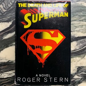May include: A novel titled "The Death and Life of Superman" by Roger Stern. The book cover is black with the Superman logo in red and yellow. The title is in yellow and red.
