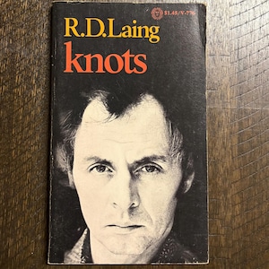 May include: Vintage paperback book titled "Knots" by R.D. Laing. The cover features a black and white portrait of a man with the title in orange and the author's name in yellow. The book has a price tag of $1.45.