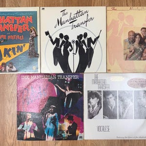 May include: A collection of five vinyl record covers by The Manhattan Transfer. The covers feature various graphic designs, including illustrations of performers, black and white silhouettes, and photographic portraits of the musical group members.
