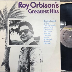 May include: A vintage vinyl record album cover for Roy Orbison's Greatest Hits. The cover features a black and white photo of Roy Orbison wearing sunglasses, with a palm tree illustration. The album title and song titles are visible.