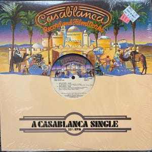 Może przedstawiać: Winyl vintage Donny Summer, zatytułowany "A Casablanca Single". Okładka albumu przedstawia kolorową ilustrację pustynnej scenerii z wielbłądami, palmami i logo Casablanca Records. Etykieta płyty jest widoczna, z tytułami piosenek i napisami.