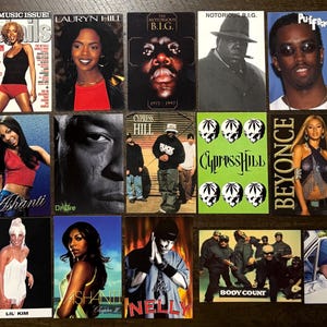 May include: A collection of rectangular trading cards featuring various hip-hop artists and music groups, including Jay-Z, Lauryn Hill, The Notorious B.I.G., Puff Daddy, Fugees, Ashanti, Cypress Hill, Beyonce, Lil Kim, Nelly, Body Count, and Eazy-E.