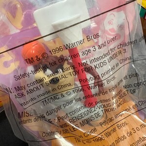 May include: A sealed plastic bag containing a vintage toy. The toy features a white basketball hoop, a red pole, and an orange basketball. The packaging includes text from 1996 Warner Bros.