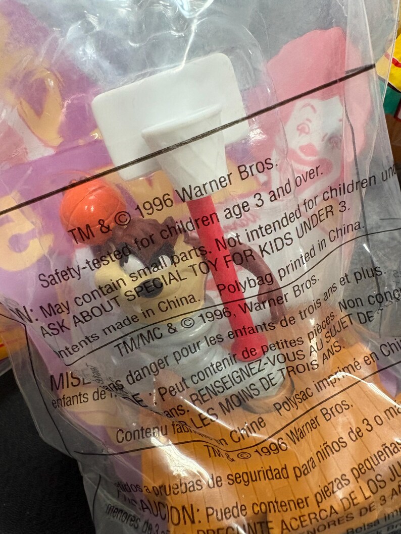 May include: A sealed plastic bag containing a vintage toy. The toy features a white basketball hoop, a red pole, and an orange basketball. The packaging includes text from 1996 Warner Bros.