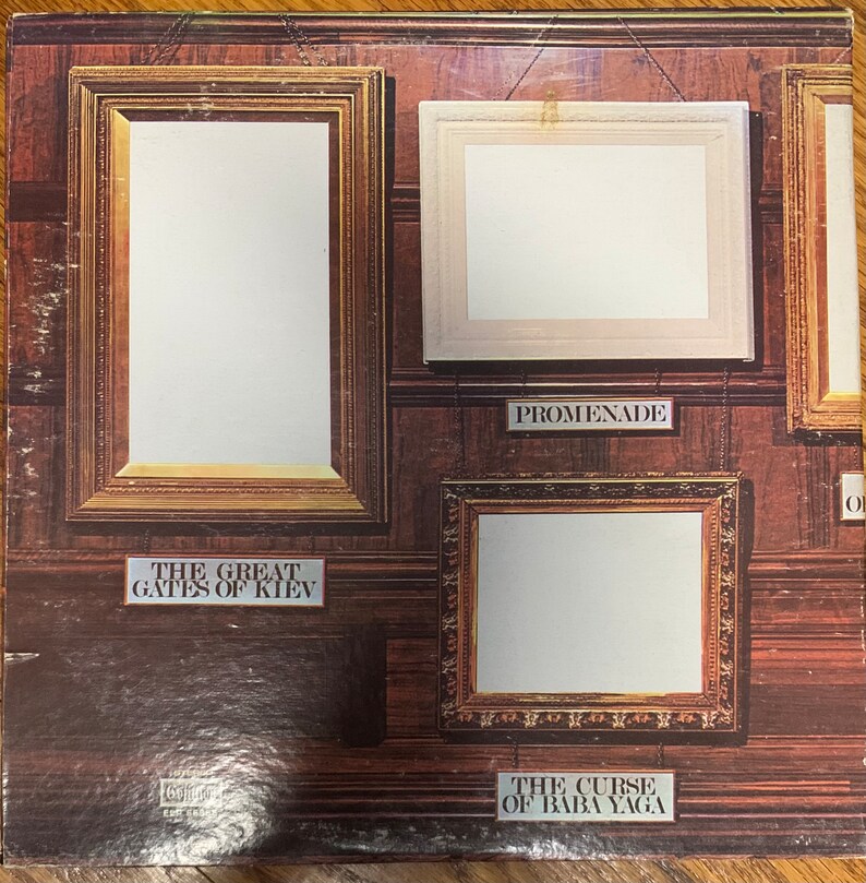 Pu&ograve; includere: Una copertina di un album vintage con uno sfondo in pannelli di legno scuro, che mostra diversi rettangoli incorniciati. Le cornici variano per dimensioni e stile, con etichette come "The Great Gates of Kiev" e "Promenade".