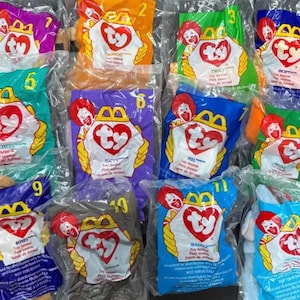May include: A collection of twelve McDonald's Ty Teenie Beanie Babies in individual plastic bags, numbered one through twelve. Each bag features a red heart-shaped Ty logo, a Ronald McDonald graphic, and a unique color background for each toy.