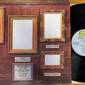 Pu&ograve; includere: Copertina dell'album "Pictures at an Exhibition" di Emerson, Lake & Palmer. L'artwork presenta cornici dorate ornate su una parete rivestita in legno, con titoli di canzoni come "The Hut of Baba Yaga" e "The Old Castle". Un disco in vinile &egrave; visibile.