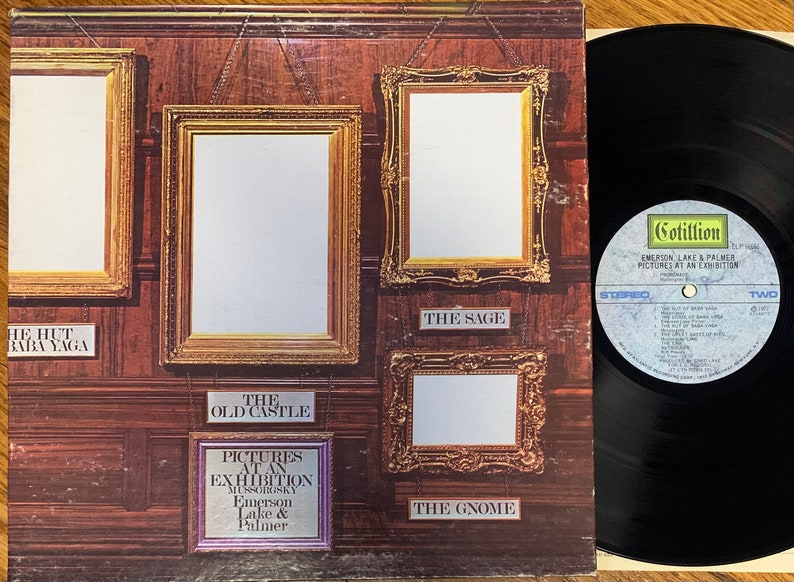 Pu&ograve; includere: Copertina dell'album "Pictures at an Exhibition" di Emerson, Lake & Palmer. L'artwork presenta cornici dorate ornate su una parete rivestita in legno, con titoli di canzoni come "The Hut of Baba Yaga" e "The Old Castle". Un disco in vinile &egrave; visibile.