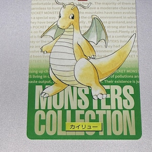May include: A rectangular trading card featuring a yellow dragon-like creature with wings and a long tail. The card displays the text POCKET MONSTER 149, MONSTERS COLLECTION, and the Japanese characters カイリュー. The background has light green text.