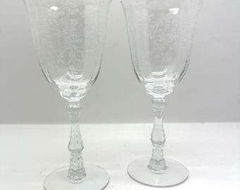 May include: Two clear glass wine glasses with etched floral designs. The glasses have a tall, slender stem and a round base.