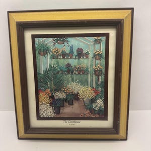 May include: A framed print of a watercolor painting depicting a greenhouse filled with various plants and flowers. The title of the painting is "The Greenhouse" by D. Saar.